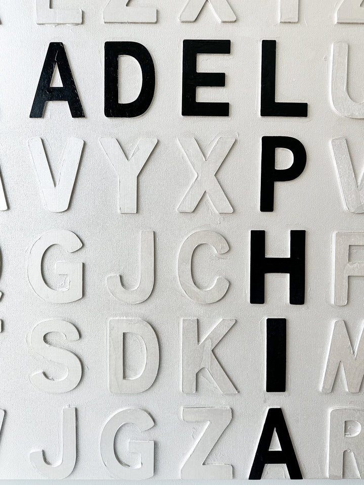 Steffanie Gerkin’s Bad Things White 3D is a contemporary mixed-media typography artwork made with raised wood and acrylic letters on canvas, featuring a white alphabet grid with bold black letters that spell “Bad Things Happen in Philadelphia.”