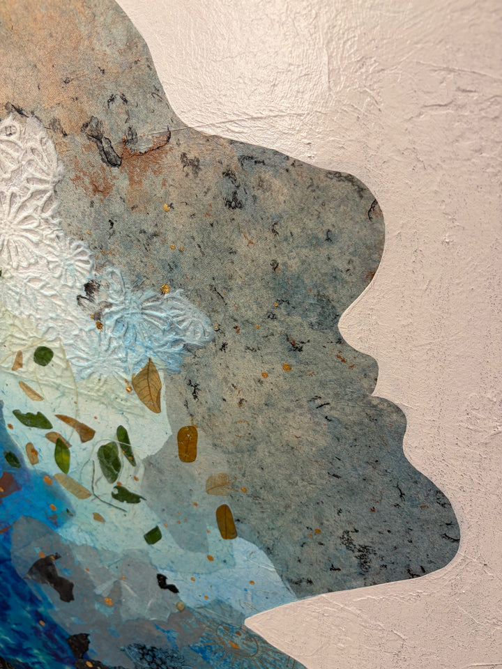 Christopher Peter, Born to Be Blue, acrylic, oil, handmade papers and gold leaf on canvas, 48 x 40 inches. Detail of the face in profile, showing gray-blue speckled handmade paper with gold leaf flecks, white embossed floral paper, and small green and brown leaves against the textured off-white canvas.