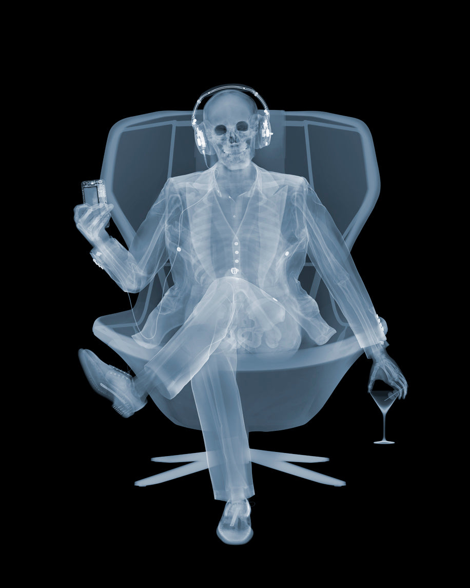 Framed Chromaluxe x-ray photograph by Nick Veasey of a skeleton listening to music with headphones in a swivel chair with a martini