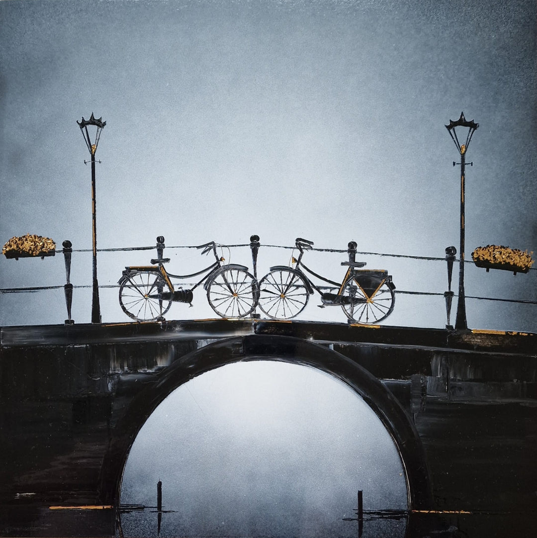 Two bikes facing each other that are parked on top of a beautiful bridge over a river with light posts and flower baskets. Painted with black and white Chinese lacquer and gold leaf by Julien Rey. The gold highlights the light in the piece.