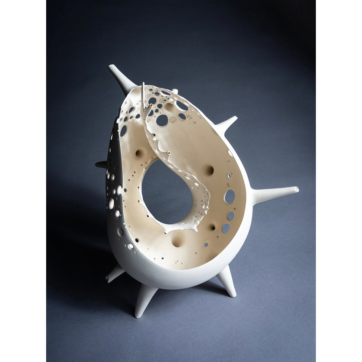 o shaped ceramic sculpture with holes and legs to stand, edges fraying shadows cast negative space