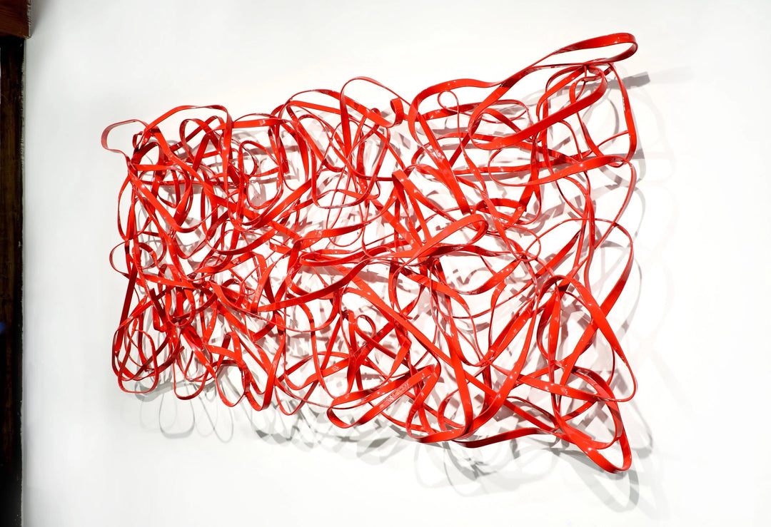 Matt Devine, 1984, powder-coated aluminum, made to order from 11 to 84 inches. Horizontal rectangular wall sculpture of thin red aluminum ribbons bent into tangled, overlapping loops on a white wall.