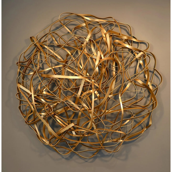 Matt Devine, 1984, powder-coated aluminum, made to order from 11 to 84 inches. Round wall sculpture of thin gold aluminum ribbons bent into tangled, overlapping loops on a taupe wall.