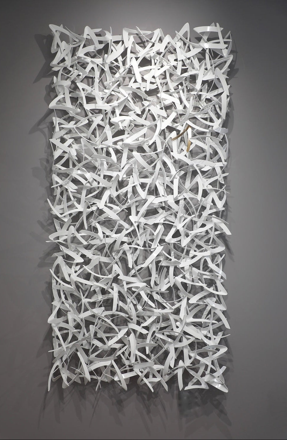Matt Devine, Avian, powder-coated aluminum, made to order from 11 to 84 inches. Tall vertical rectangular wall sculpture of many small, curved white aluminum pieces shaped like bird wings, interlocked in a dense field on a grey wall.