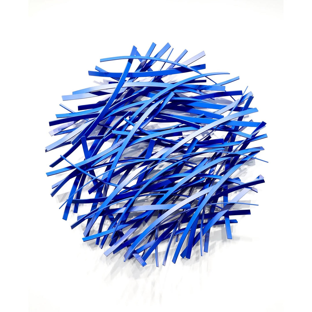 Matt Devine, Thin Bands, powder-coated aluminum, made to order from 11 to 84 inches. Round wall sculpture of thin, curved aluminum strips in royal blue, navy, and light blue, layered in a dense crisscross pattern on a white wall.