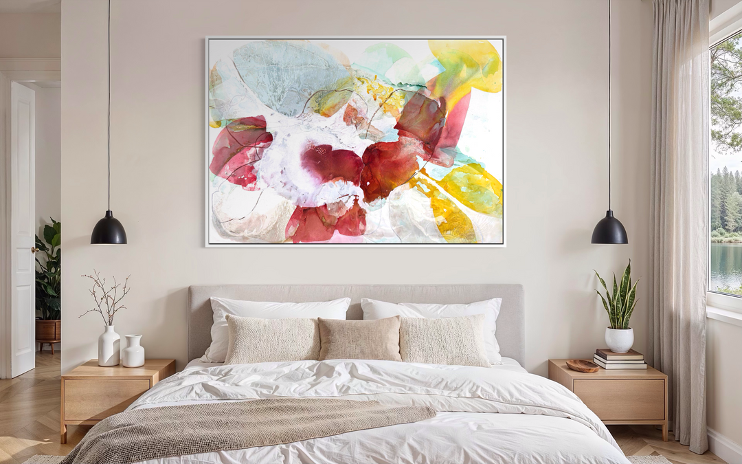 Liz Barber, Tide Pool 2, acrylic paint, ink, watercolor, and graphite on canvas, 72 x 50 inches. Horizontal abstract composition of overlapping translucent shapes in crimson, rose pink, golden yellow, pale blue, and white with fine graphite lines around a white center, shown in a white frame above a bed with a beige upholstered headboard between two black pendant lights.