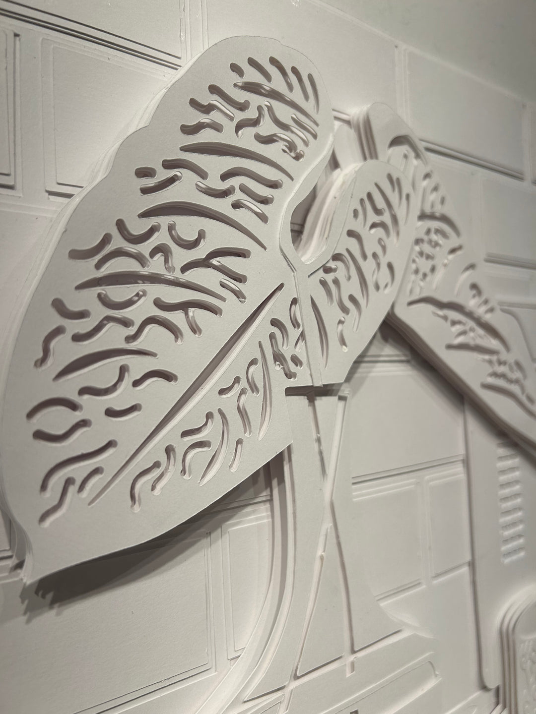 14"x14" layered white paper forming a a vase with leaves on a wall. 