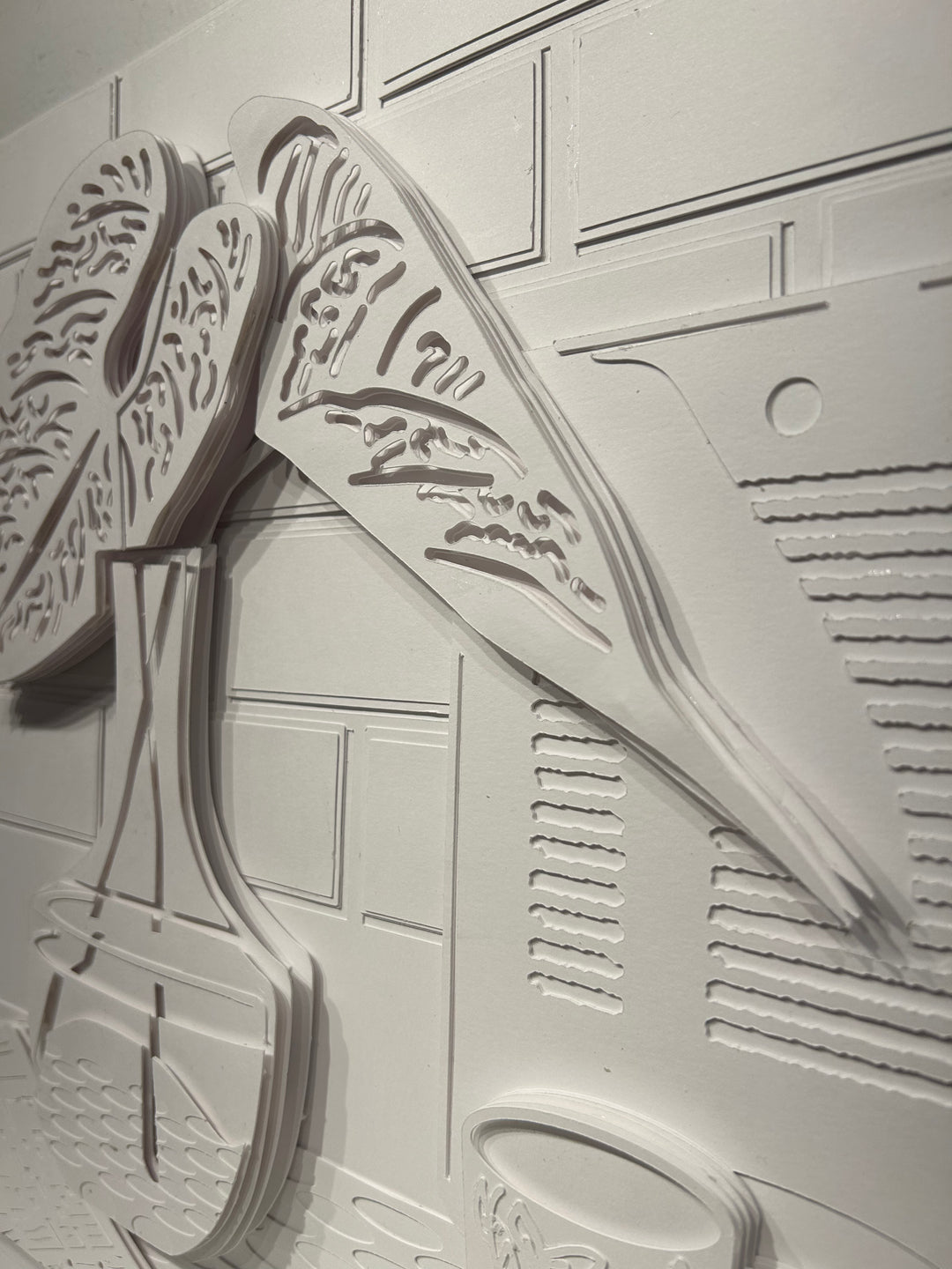 14"x14" layered white paper forming a a vase with leaves on a wall. 